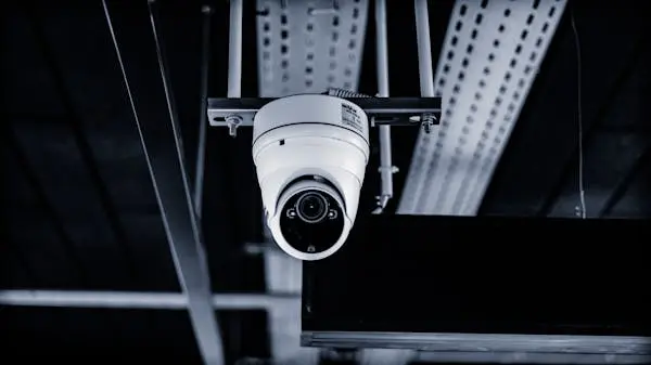 White dome-style store security camera hanging from a dark ceiling indoors