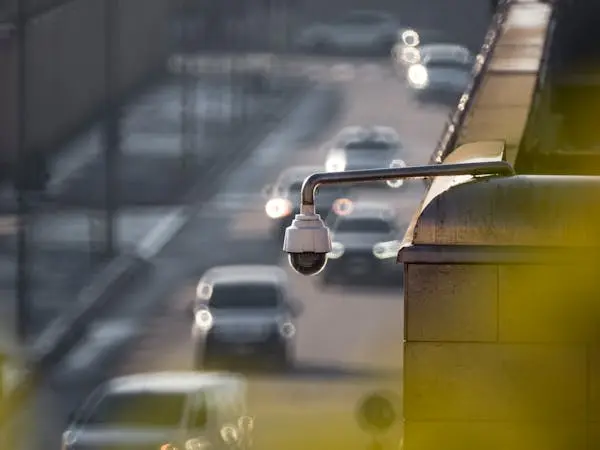 A store security camera mounted on a bridge overpass overlooking traffic below