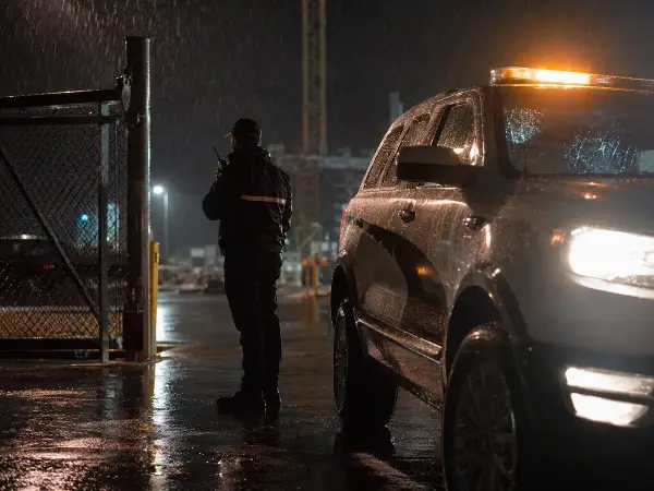 Security officer responding at a construction gate at night beside a patrol vehicle