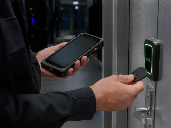 Officer logging a patrol checkpoint on a GPS guard-tour device at a data center