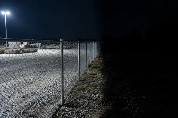 Perimeter fence line where floodlight coverage ends and darkness begins
