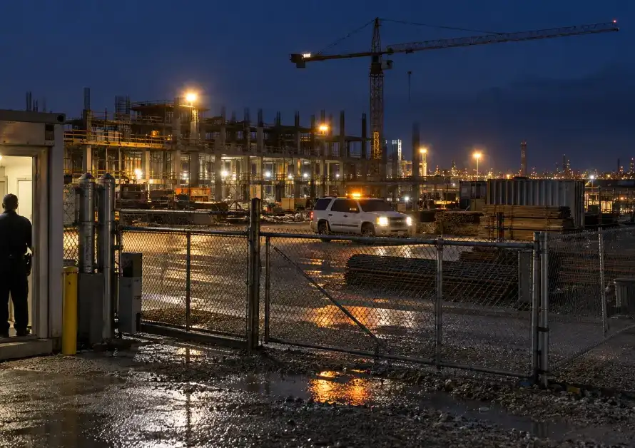Static guard post at a construction site gate while a roving guard's vehicle patrols the fence line at night